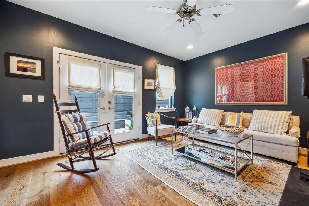 This inviting living room features dark blue walls, hardwood floors. Large French doors allow natural light to fill the space, complemented by a ceiling fan for added comfort.