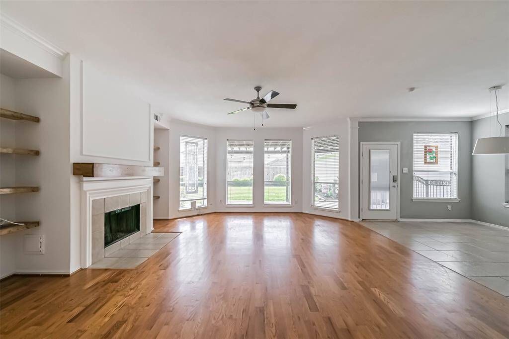 This spacious living area features hardwood floors, a cozy fireplace, and abundant natural light from large windows. It seamlessly connects to the dining area with tile flooring, offering easy access to the backyard through a glass door.