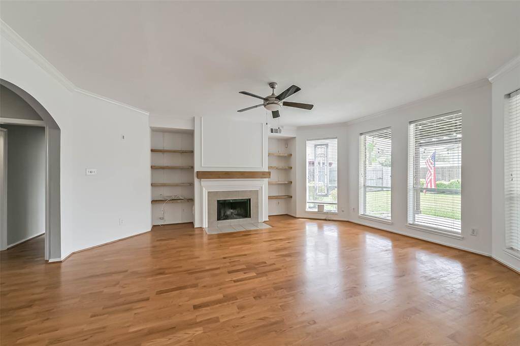 This spacious living room features hardwood floors, a cozy fireplace, built-in shelving, and large windows offering plenty of natural light and garden views.