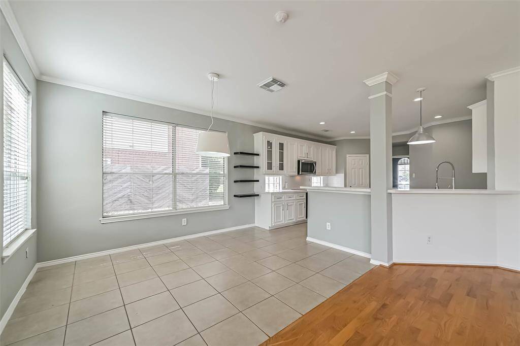 Bright, open-plan room with large windows, combining kitchen and dining areas. The kitchen features white cabinets, modern appliances, and a breakfast bar. Neutral tones and mixed flooring enhance the spacious feel.