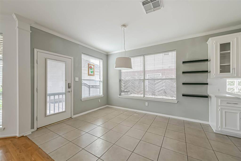 Bright and airy room with large windows covered by blinds, featuring tile flooring. It includes a door leading outside, a hanging light fixture, and built-in shelves. Perfect for a cozy dining area or sunlit sitting room.