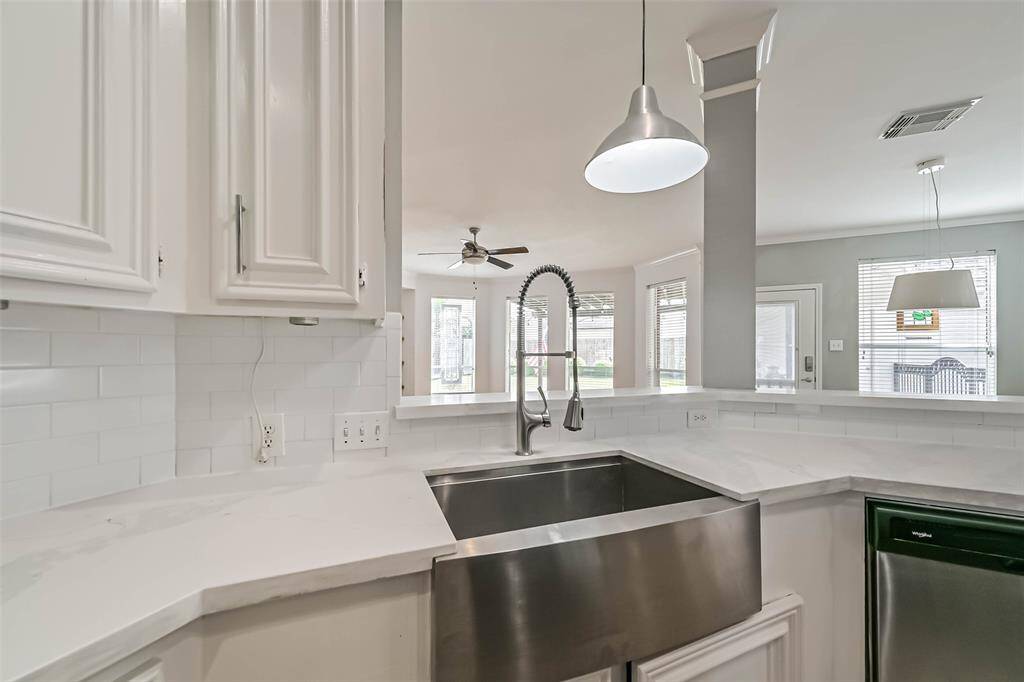 Modern kitchen with white cabinetry, stainless steel farmhouse sink, and sleek fixtures. Features an open layout with a view of the living area, pendant lighting, and ample natural light through large windows.