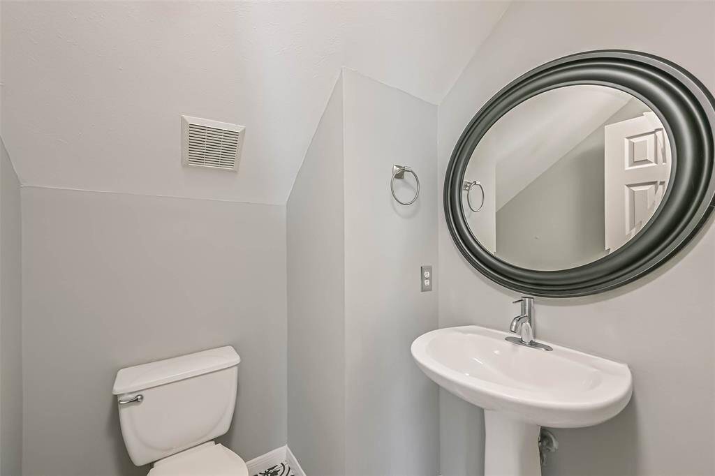 This photo shows a small, modern half-bathroom with light gray walls. It features a white pedestal sink with a sleek, black-framed oval mirror above it. There's a toilet tucked under a sloped ceiling, providing a cozy yet functional space.