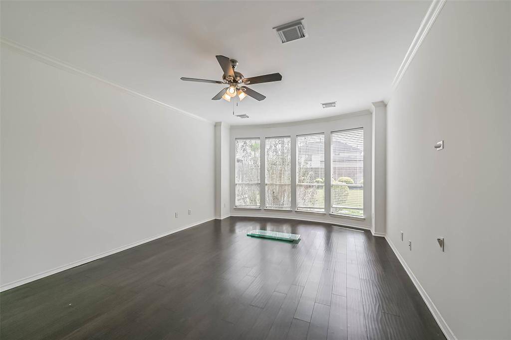 This room features dark hardwood floors, a ceiling fan, and a large bay window that provides abundant natural light, ideal for a living or sitting area.