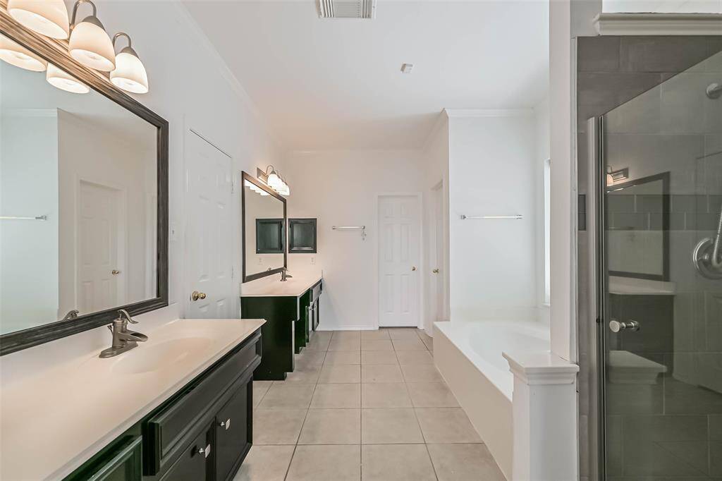 This is a spacious, modern bathroom featuring dual sinks with large mirrors, a separate glass-enclosed shower, and a built-in bathtub. The neutral color palette and ample lighting create a bright and inviting atmosphere.