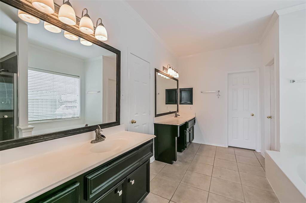This bathroom features dual sinks with dark cabinetry, large mirrors, and stylish lighting. It has a bright, spacious feel with neutral tiles and a window for natural light.