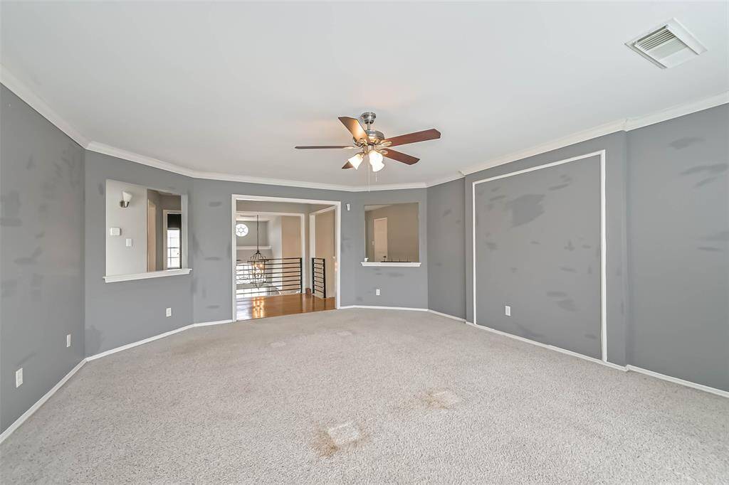 Spacious room with neutral gray walls, carpeted flooring, and a ceiling fan. Features two open wall cutouts for a modern touch, leading to a hallway with wood flooring and railings. Ideal for a versatile living space.
