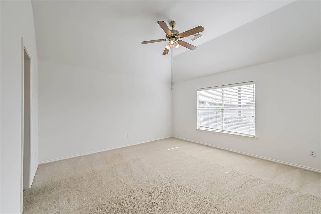 This spacious bedroom features a vaulted ceiling with a fan, neutral carpet, and a large window providing ample natural light.