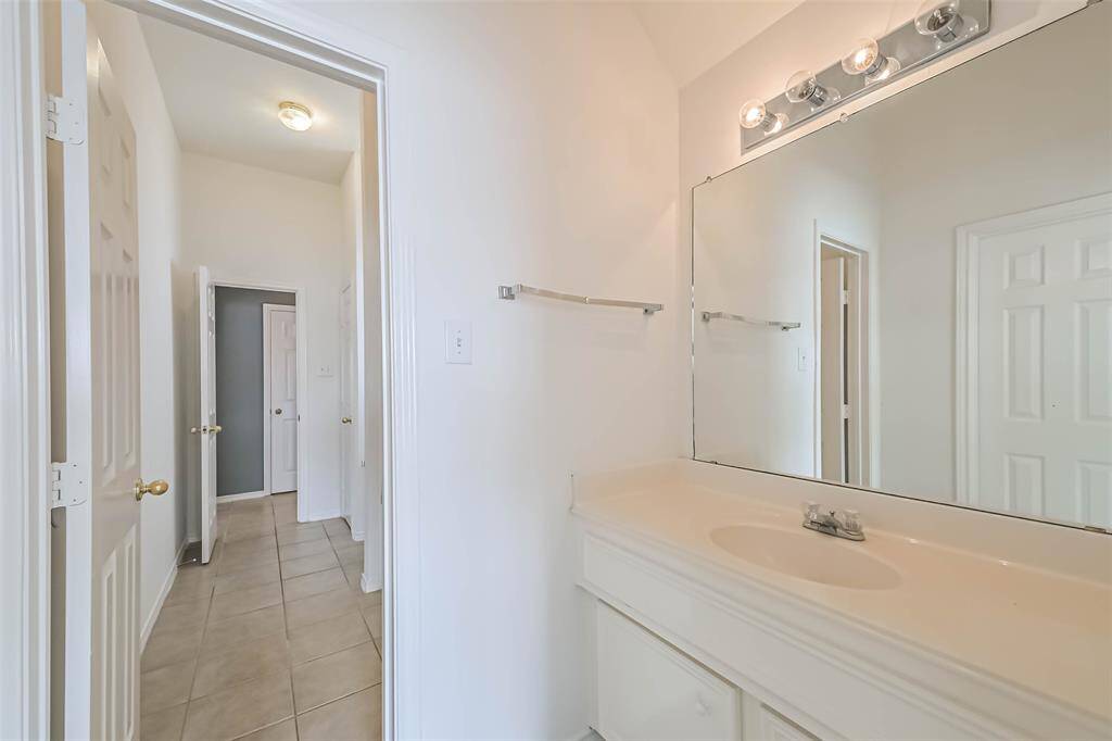Bright bathroom featuring a large mirror, ample counter space, and a hallway view.