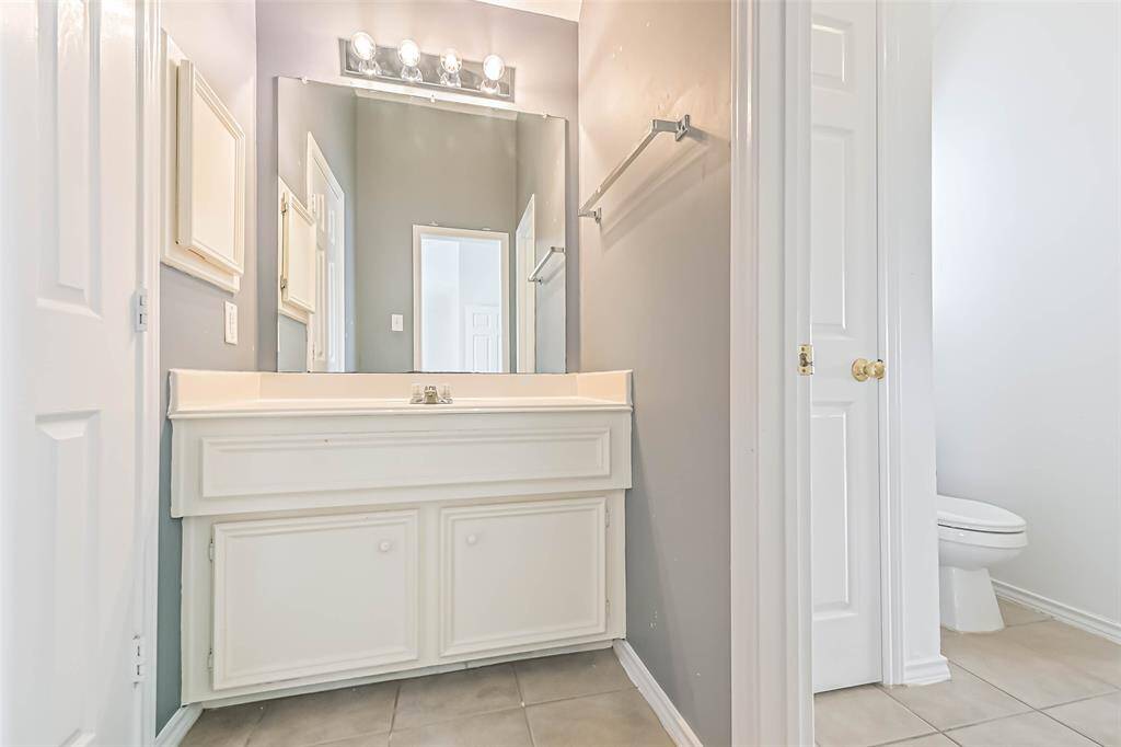 This bathroom features a clean, modern design with a large mirror, vanity with ample storage, and a separate toilet area. Neutral tones and tile flooring create a bright, inviting space.