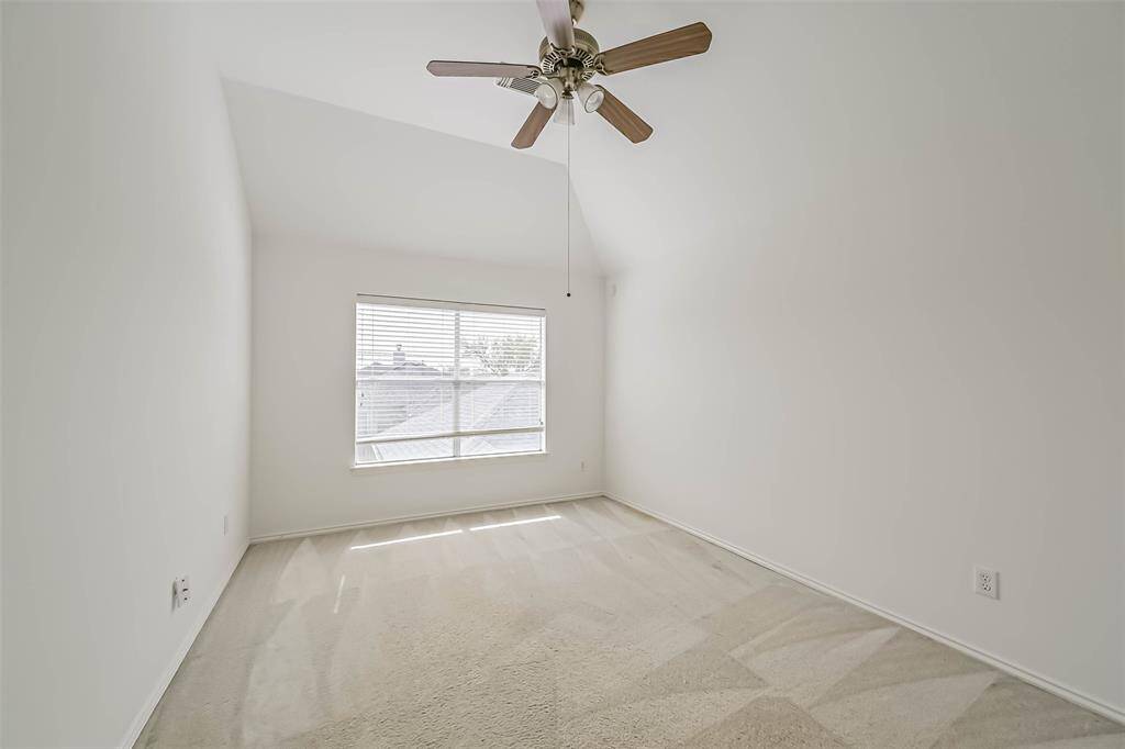 Bright, airy bedroom with vaulted ceiling, ceiling fan, and large window providing ample natural light. Neutral carpet and walls offer a versatile decor palette.