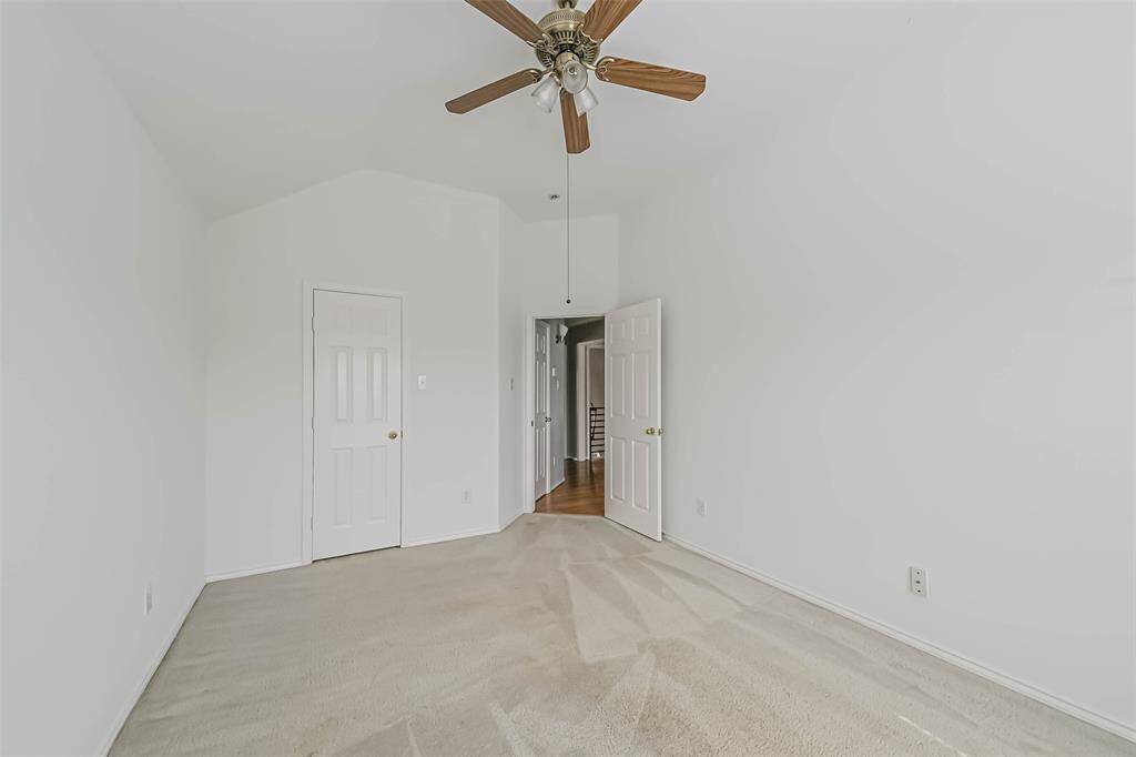 This photo shows a bright, empty bedroom with clean white walls, a neutral carpet, and a ceiling fan. There are two doors, one leading to another room, and the space feels open and ready for personalization.