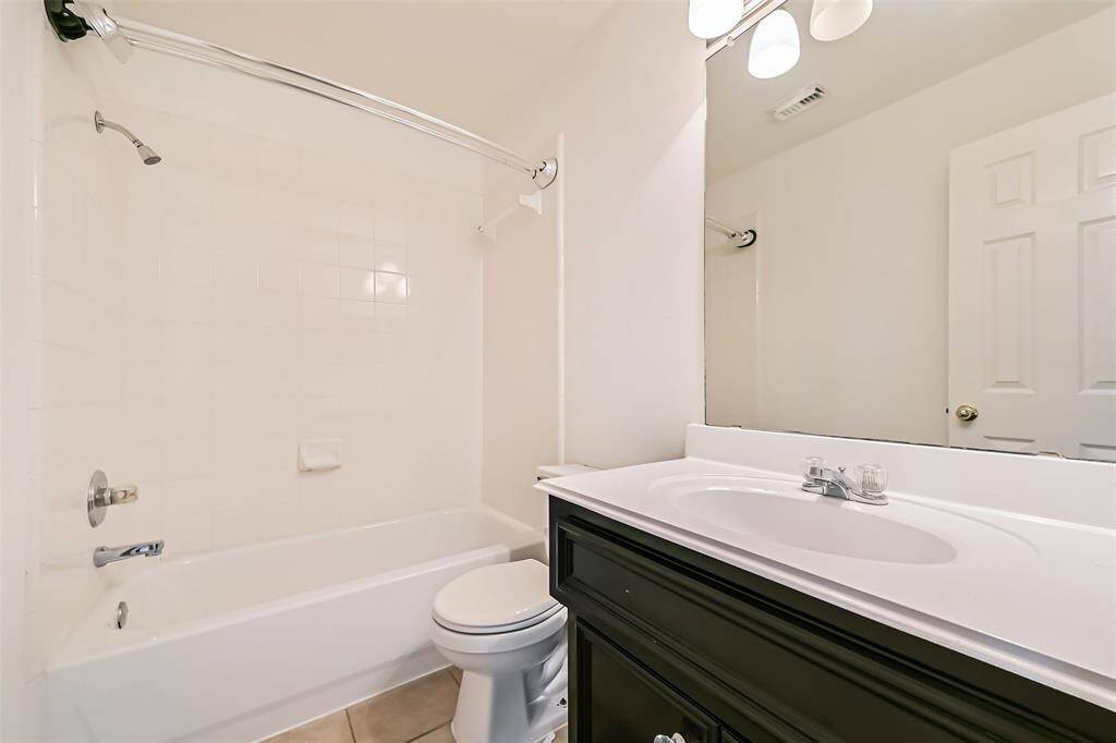This is a clean, modern bathroom featuring a white bathtub with a shower, a sleek black vanity with a white countertop, and a large mirror. The space is well-lit with overhead lights, and neutral tiles add to the bright, airy feel.