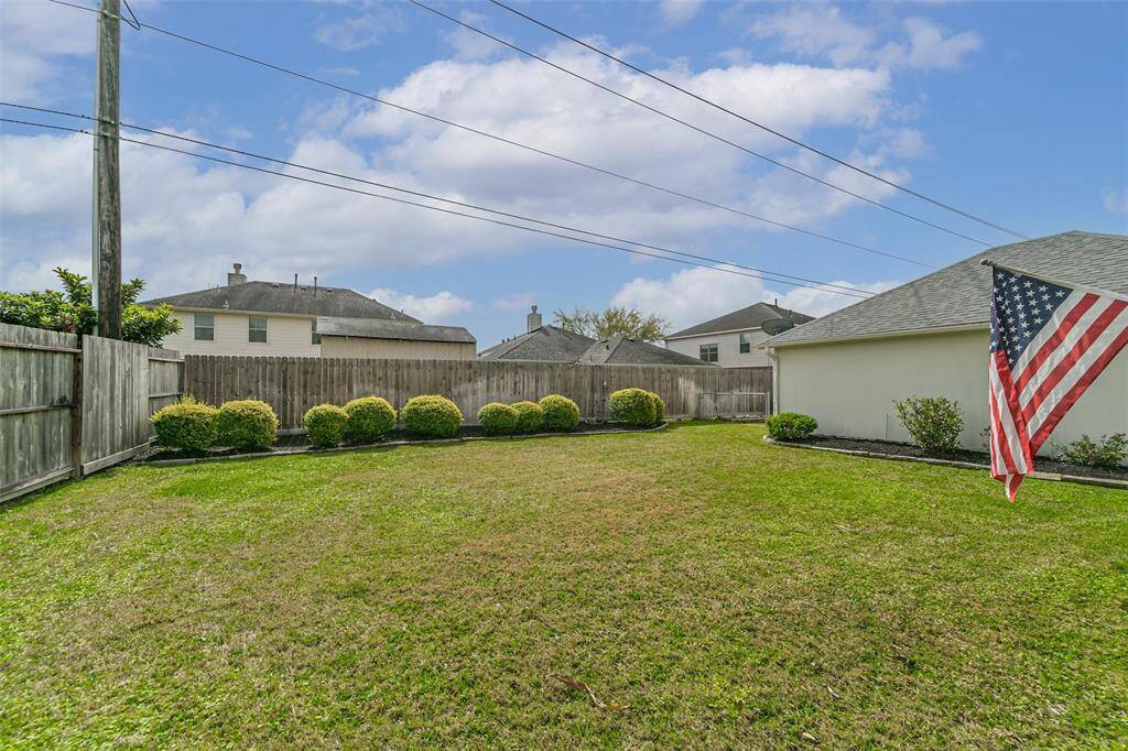 Spacious backyard with a well-maintained lawn, surrounded by a wooden fence for privacy. Includes neatly trimmed shrubs and a garage with an American flag. Ideal for outdoor activities.
