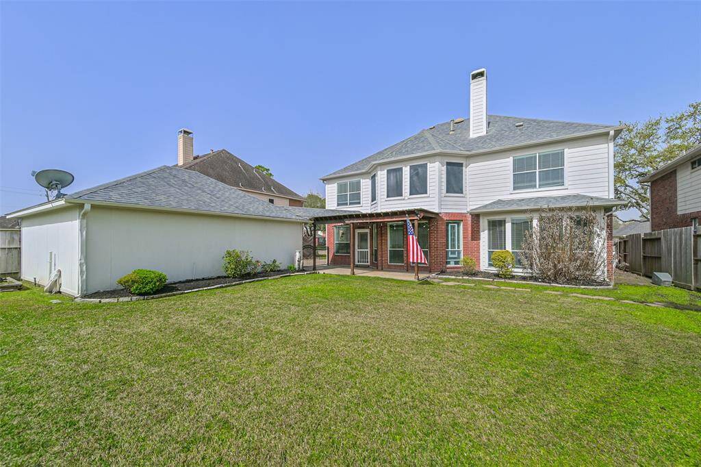This photo showcases the backyard of a two-story home with a well-maintained lawn, a detached garage, and a covered patio area. The exterior features a combination of brick and siding, with large windows providing plenty of natural light.