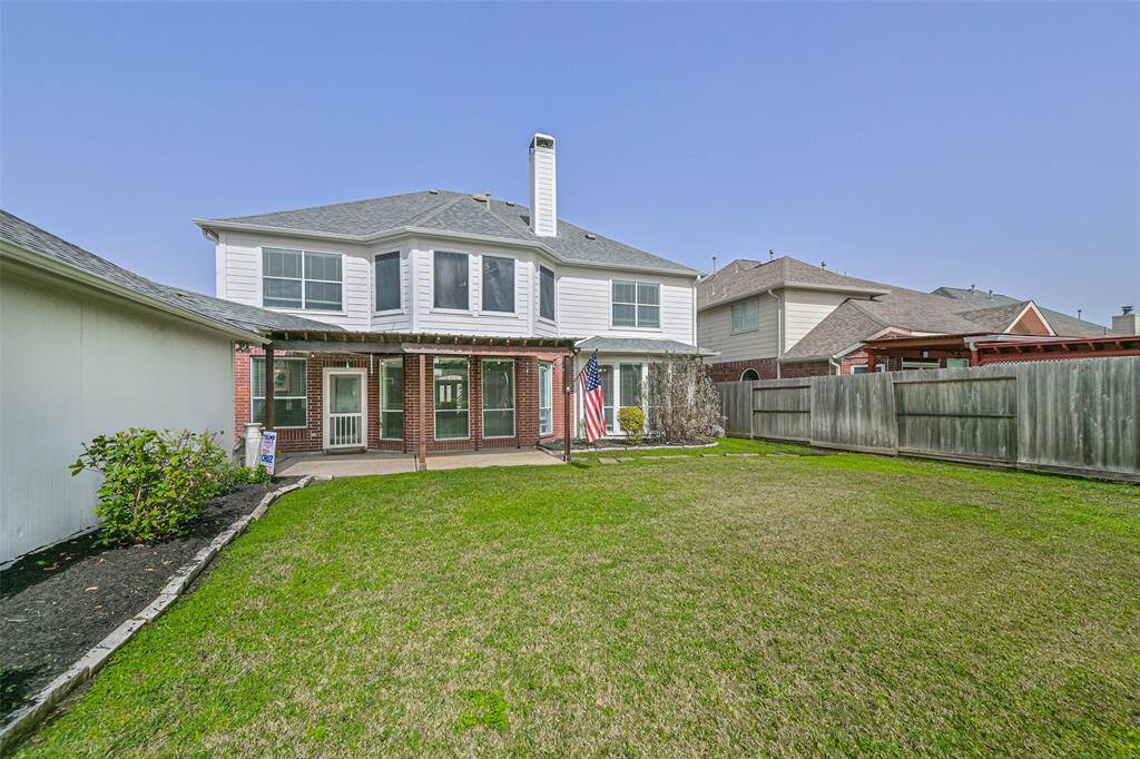 This photo showcases a spacious backyard with a well-maintained lawn and a two-story house featuring large windows and a covered patio. The yard is enclosed by a wooden fence, providing privacy, and there's a small garden bed on one side.
