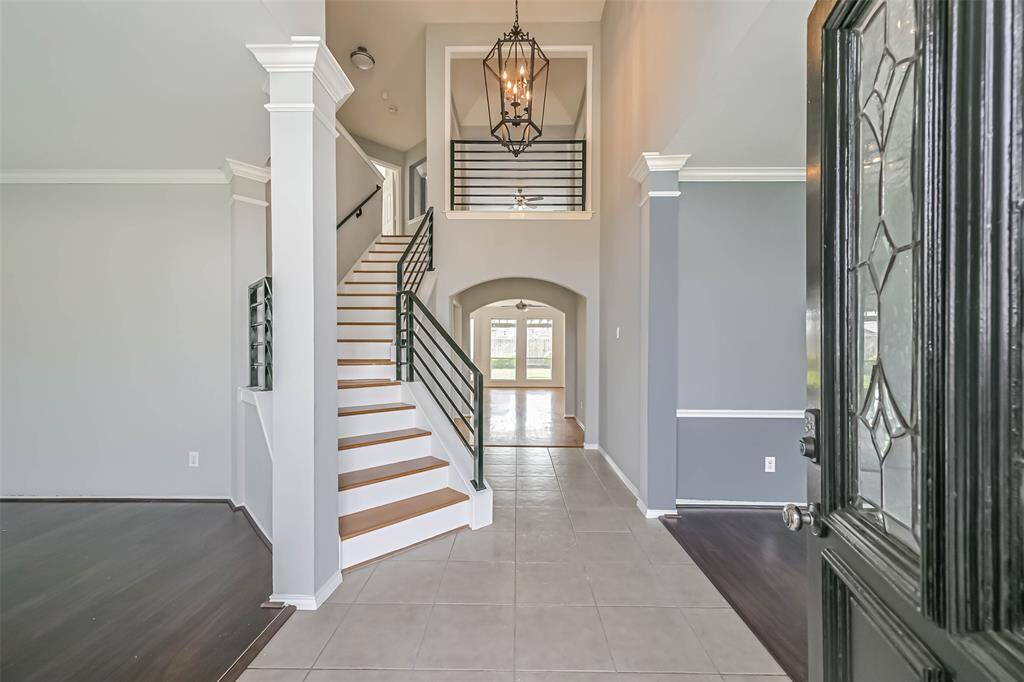 This photo showcases a bright and inviting entryway with high ceilings, a grand staircase, and modern finishes. The space features a mix of tile and hardwood flooring, elegant light fixtures, and an open view to additional living areas.