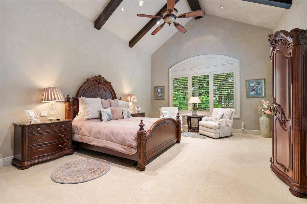 The primary suite boasts a vaulted, beamed ceiling and offers serene, private views of the backyard, showcasing mature trees and a sparkling pool.