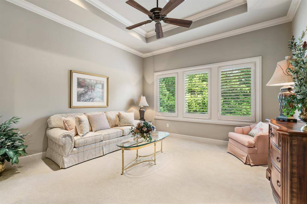 One of two additional oversized en suite bedrooms upstairs features neutral carpeting and a stunning wall of windows overlooking a serene, tree-lined backdrop.