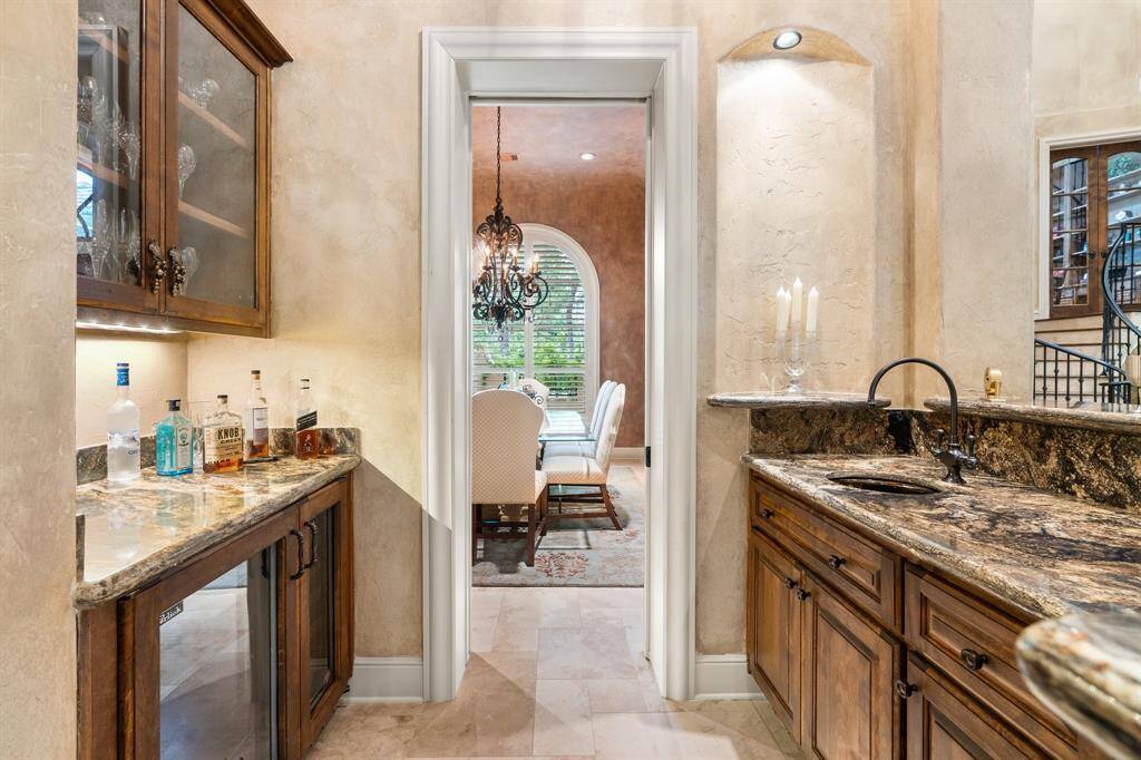 The bar with rich wood cabinetry, granite counters, fridge and wine chiller, is central to the formal living spaces and kitchen.