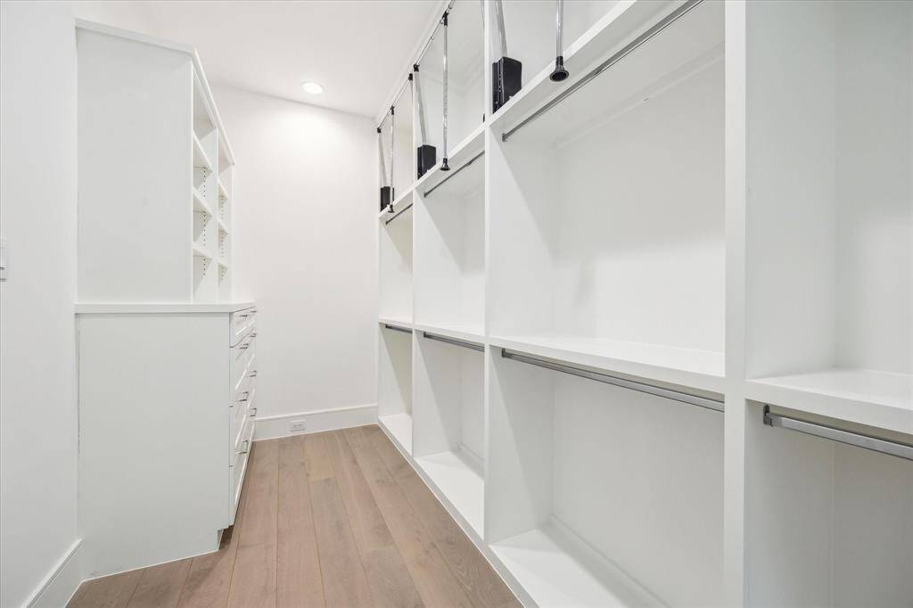 Spacious primary closet features built-in storage and ample room for hanging clothes with pull-down bars for accessing all custom storage solutions.