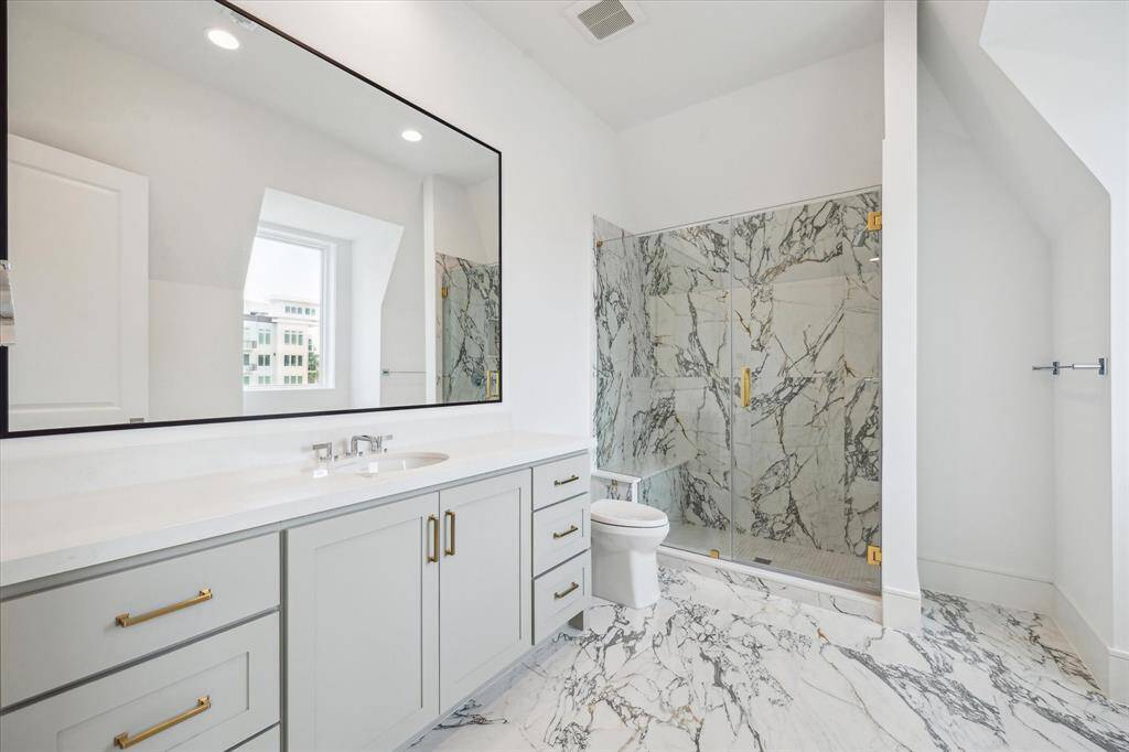 Oversized bathroom features glass-framed walk-in shower with niche, expansive mirror, and excess storage and counter space.