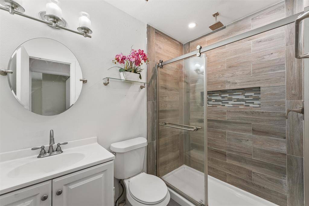 Featuring wood-look tile, a rainfall showerhead, and sleek glass doors, this updated bathroom blends warmth with modern elegance—perfect for your daily reset.