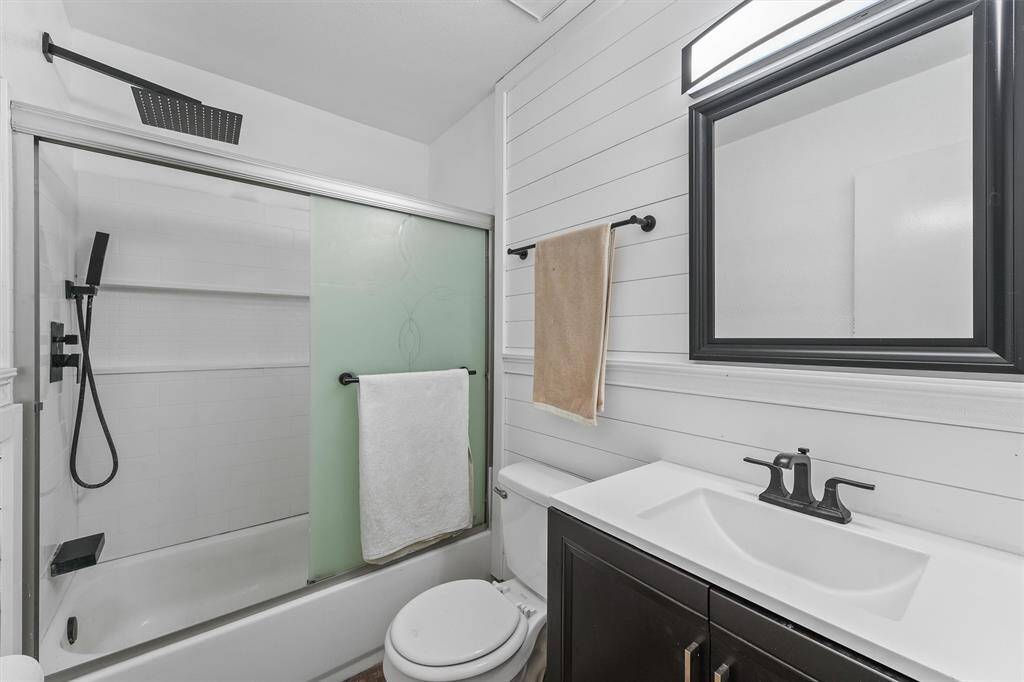 This en-suite bath features sleek black fixtures, a rainfall showerhead, and charming faux shiplap detail that adds warmth and texture without the fuss.
