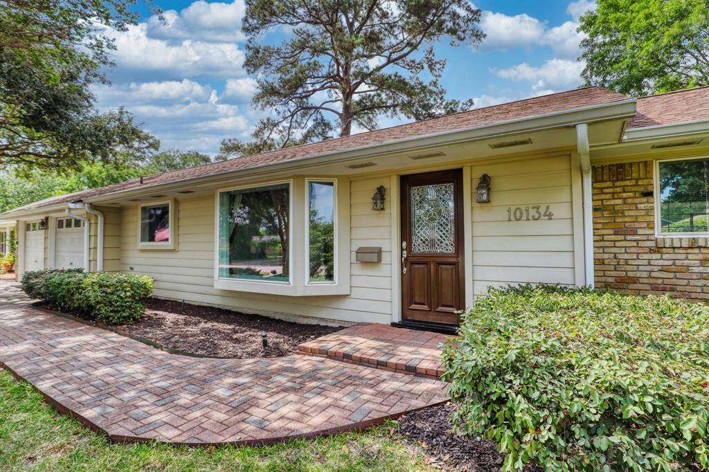 Charming single-story home with a welcoming brick walkway, large front windows, and a decorative front door. Surrounded by lush greenery, it offers a cozy and inviting curb appeal.