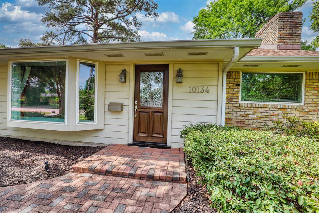 A welcoming brick walkway and lush landscaping. Features large windows for natural light, a decorative wooden front door, and a cozy brick chimney. Ideal for those seeking a blend of classic and modern appeal.
