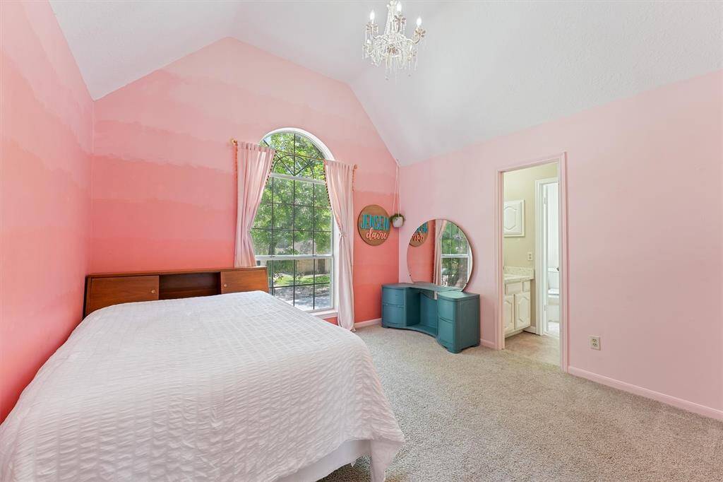 This secondary bedroom is the perfect example of how to combine comfort, style, and convenience. With its high vaulted ceiling, vibrantly painted pink walls, and spacious arched window, there's plenty of light and space.