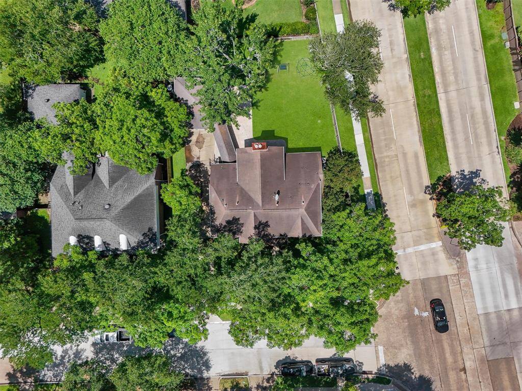 A charming home nestled among lush trees, providing ample privacy. The property features a well-maintained yard and is situated in a quiet neighborhood with nearby roads. A swimming pool is visible in a neighboring yard, highlighting the family-friendly environment.