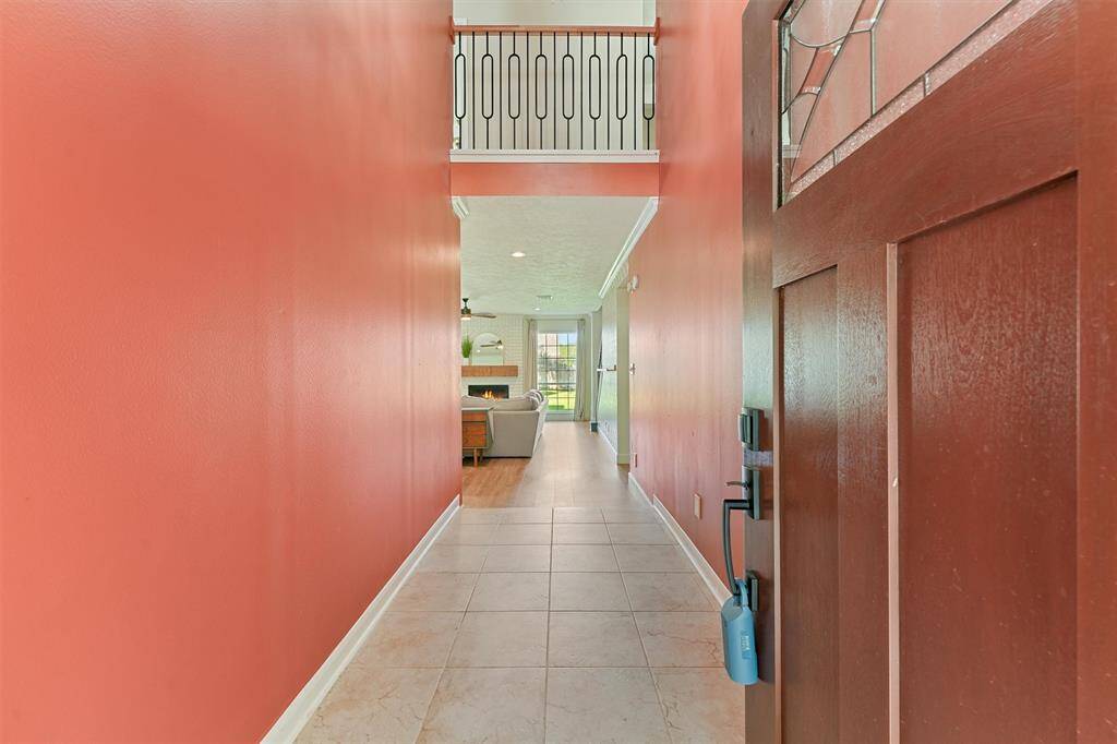 When entering feel the warmth from the coral-painted entryway leading to a bright living room with a cozy fireplace. The tiled hallway and modern railing above add a touch of elegance. Perfect for comfortable living.