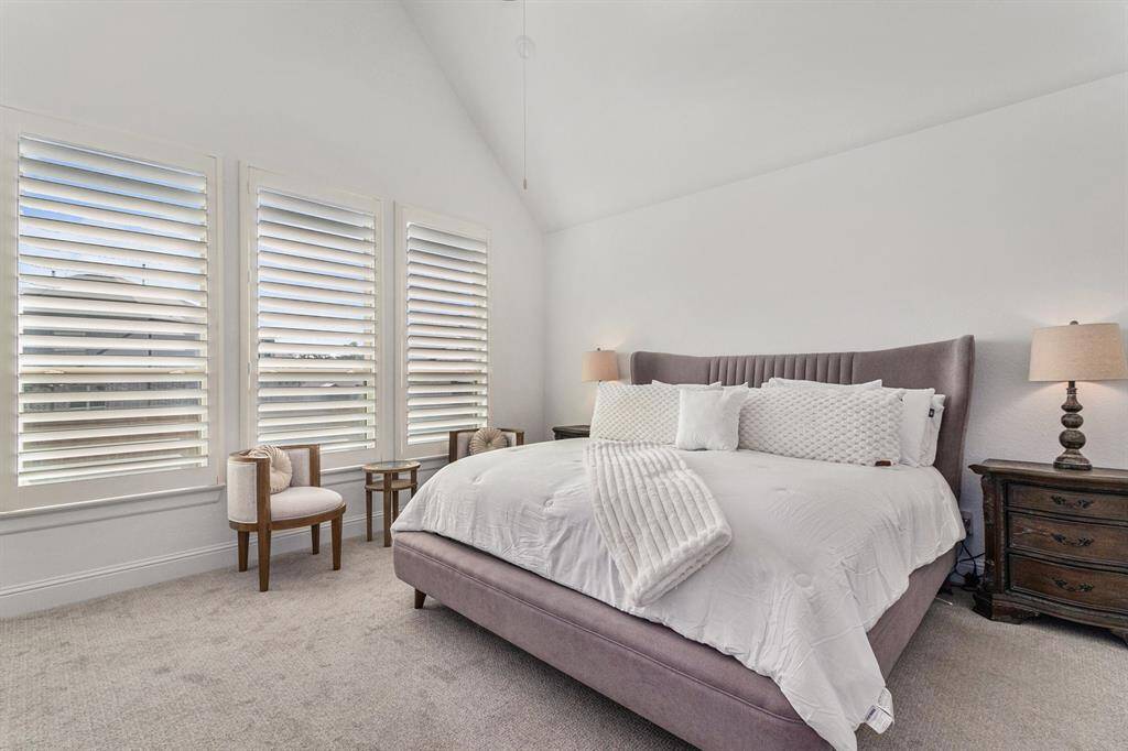 Spacious primary bedroom featuring abundant natural light, elegant shutters, and a cozy plush bed for ultimate relaxation.