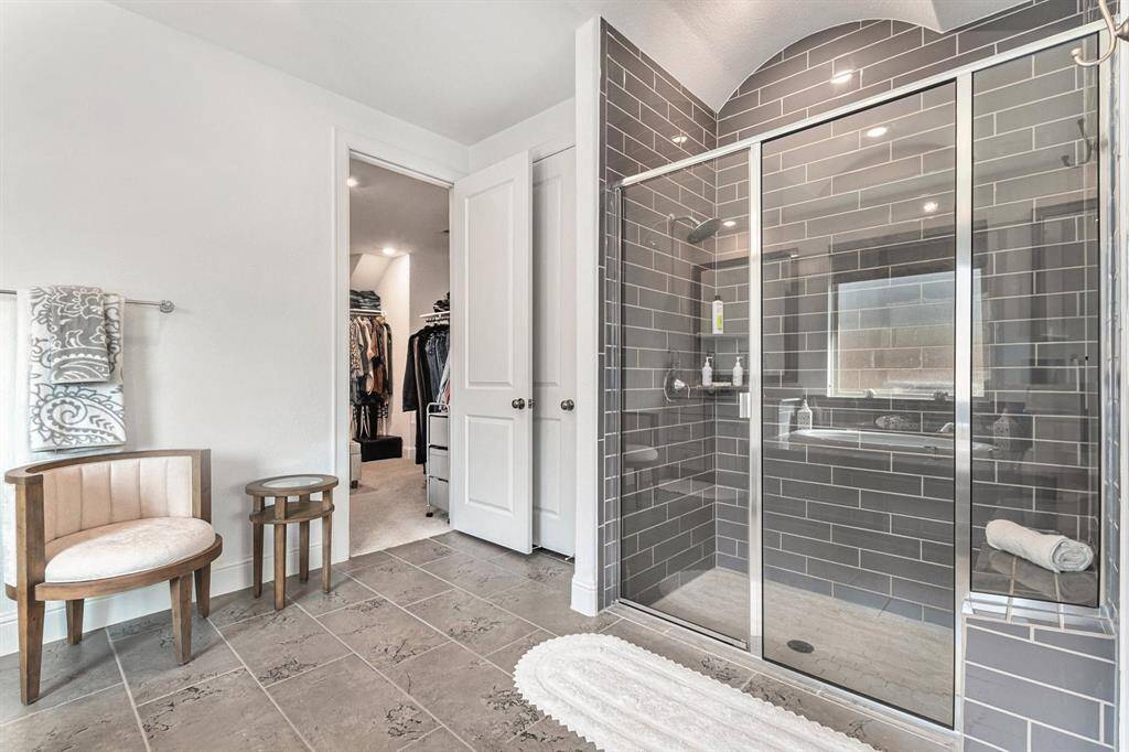 Luxurious primary bathroom featuring a sleek glass-enclosed shower, elegant tilework, and direct access to a spacious walk-in closet. Perfect for relaxation and convenience.