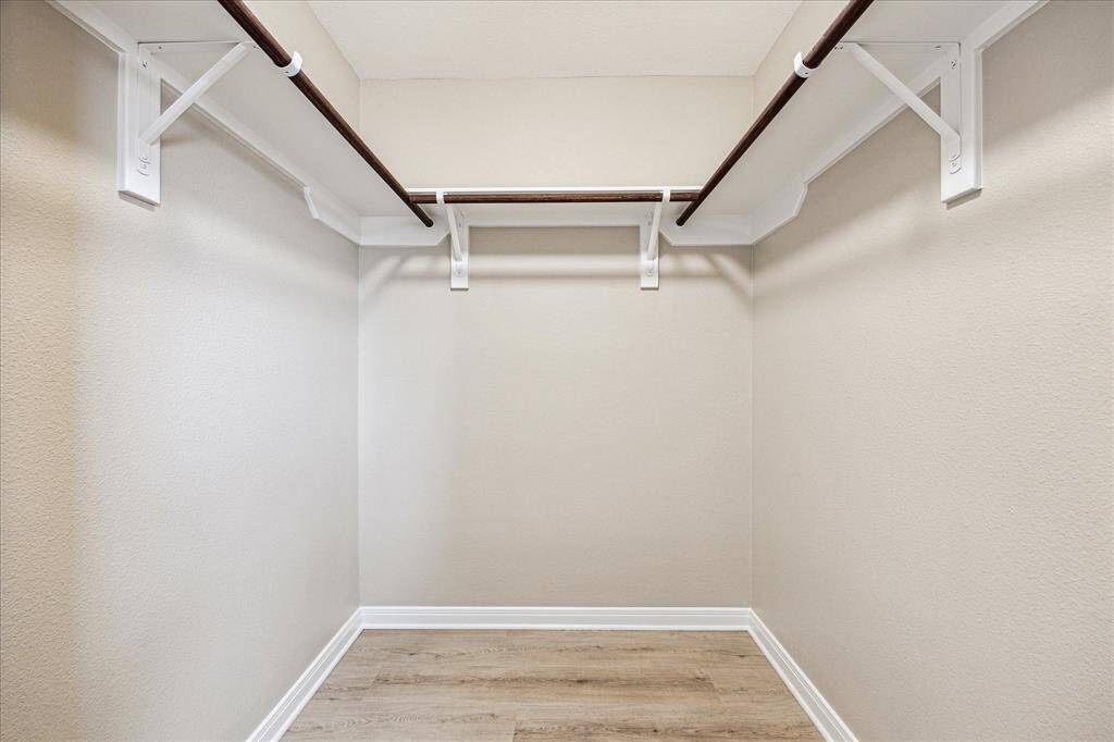 Spacious walk-in closet with light beige walls, vinyl wood flooring, and dual hanging rods for ample storage.
