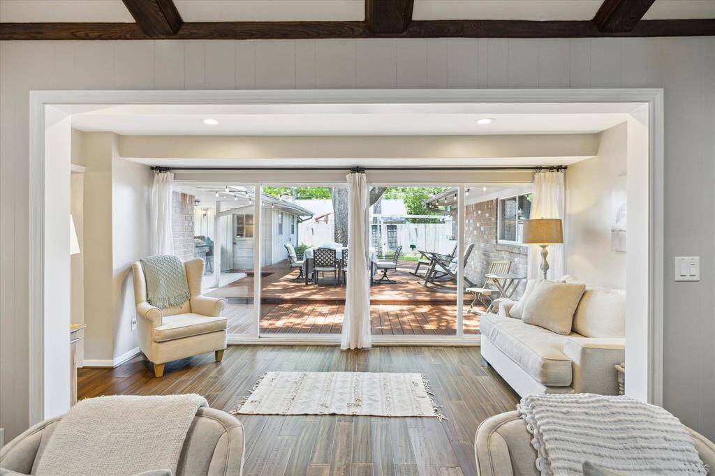 This inviting sun room features warm wood floors, cozy seating, and large sliding glass doors that open to a spacious deck, perfect for indoor-outdoor living.