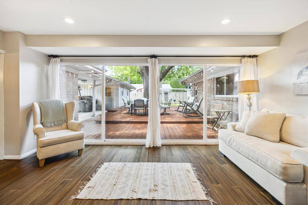 This photo showcases a cozy sun room with warm wood flooring and a sliding glass door leading to a spacious, inviting deck. Natural light floods the room, highlighting a comfortable armchair and sofa, perfect for relaxing or entertaining.