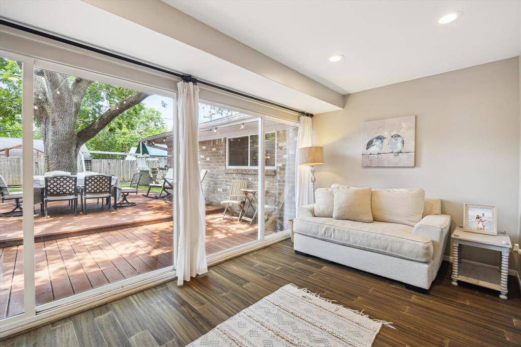 The sun room features large sliding glass doors leading to a wooden deck, perfect for outdoor dining. A comfortable sofa and tasteful decor create a welcoming atmosphere, while natural light enhances the room's warmth.