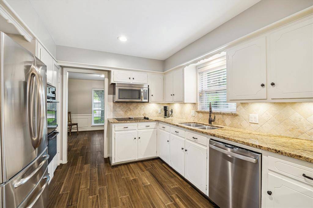 This kitchen features modern stainless steel appliances, granite countertops, and white cabinetry. The space is well-lit with ample natural light from the window over the sink.