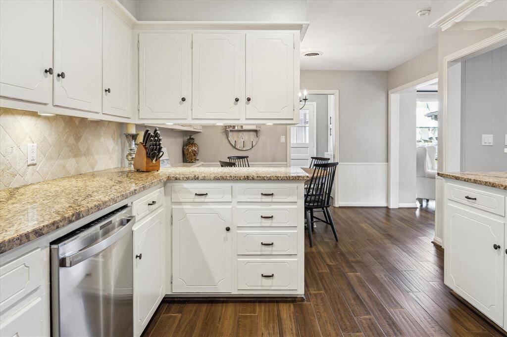 The kitchen features elegant granite countertops, classic white cabinetry, and stainless steel appliances. The engineered hardwood floors and neutral walls create a warm and inviting atmosphere, opening into a cozy dining area.