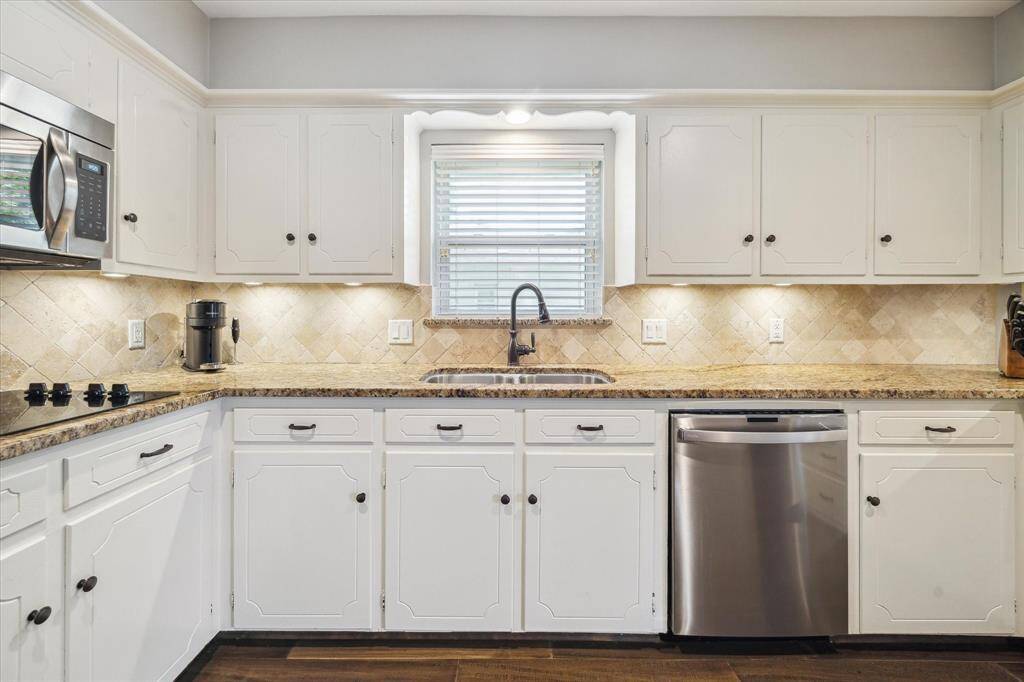 The kitchen features white cabinetry with modern hardware, granite countertops, and a tiled backsplash. It includes stainless steel appliances, a built-in microwave, and a large window above the sink for natural light.