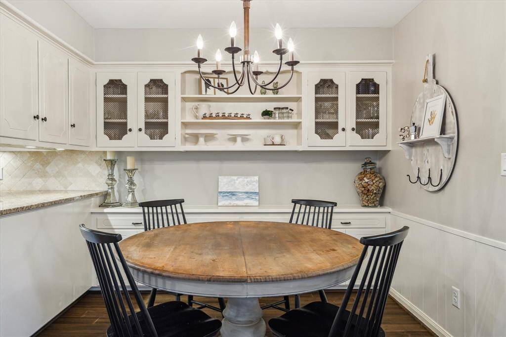 This charming dining nook features a rustic wooden table with black chairs, complemented by built-in white cabinetry with decorative glass doors. A stylish chandelier adds elegance, while open shelving and tasteful decor create a cozy, inviting atmosphere.