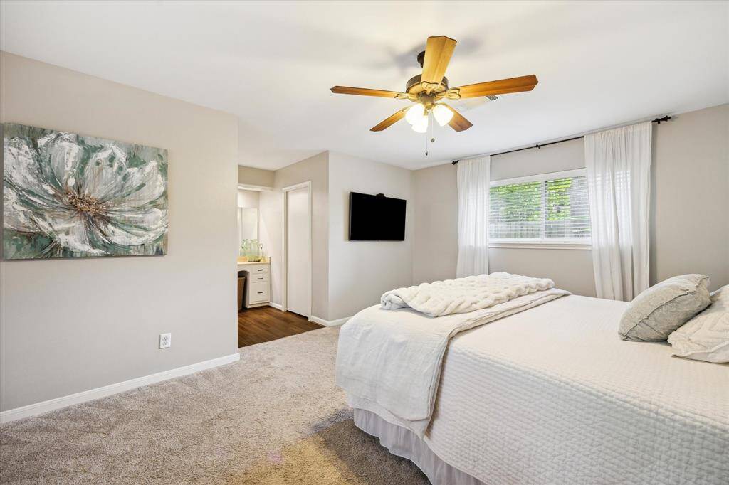 This spacious bedroom features a large window with drapes for natural light, a dedicated vanity, and a modern ensuite bathroom.