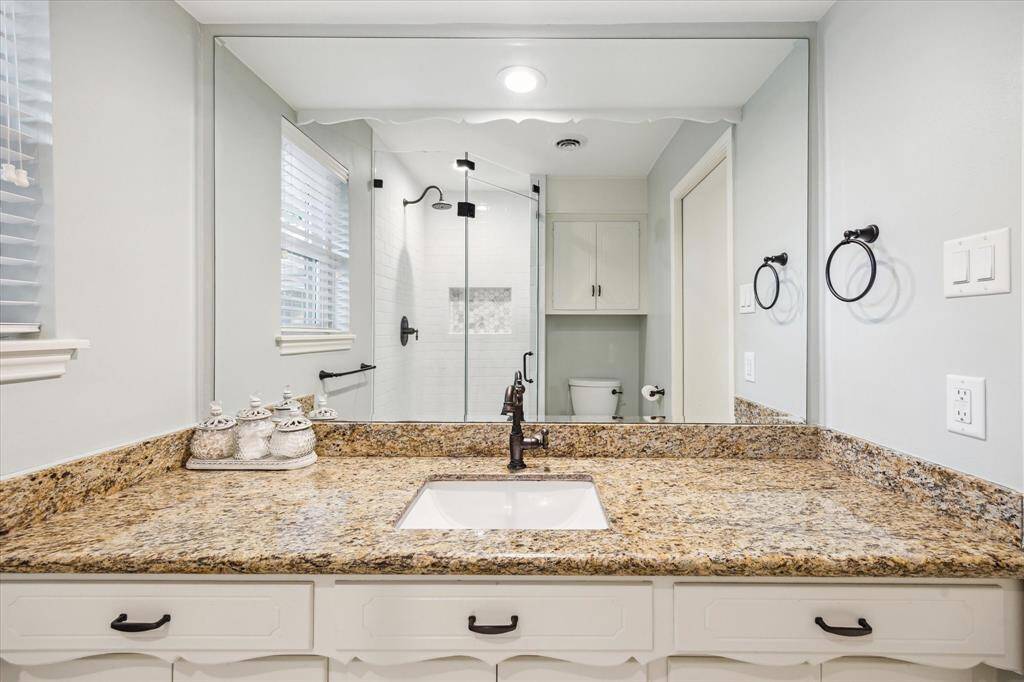 This bathroom features a granite countertop with a built-in sink, a large mirror, and a modern walk-in shower with glass doors. The space is well-lit and includes stylish fixtures.