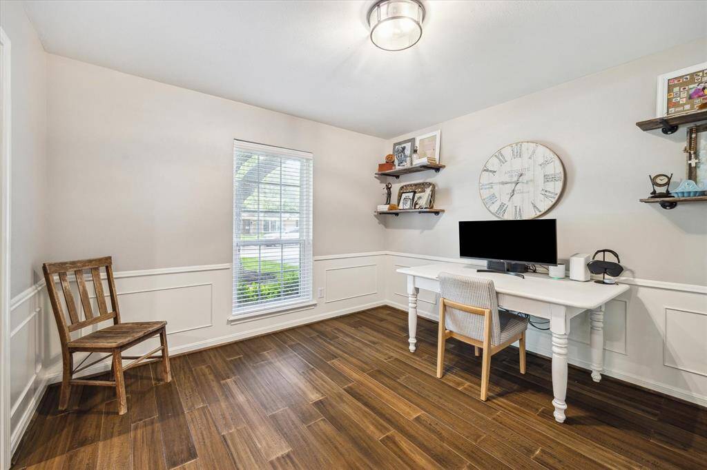 Bright home office with a large window, wood flooring, and elegant wainscoting creating a cozy and functional workspace.