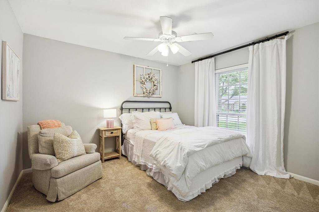 This bedroom features soft gray walls, plush carpeting, and a large window creating a serene and inviting atmosphere.