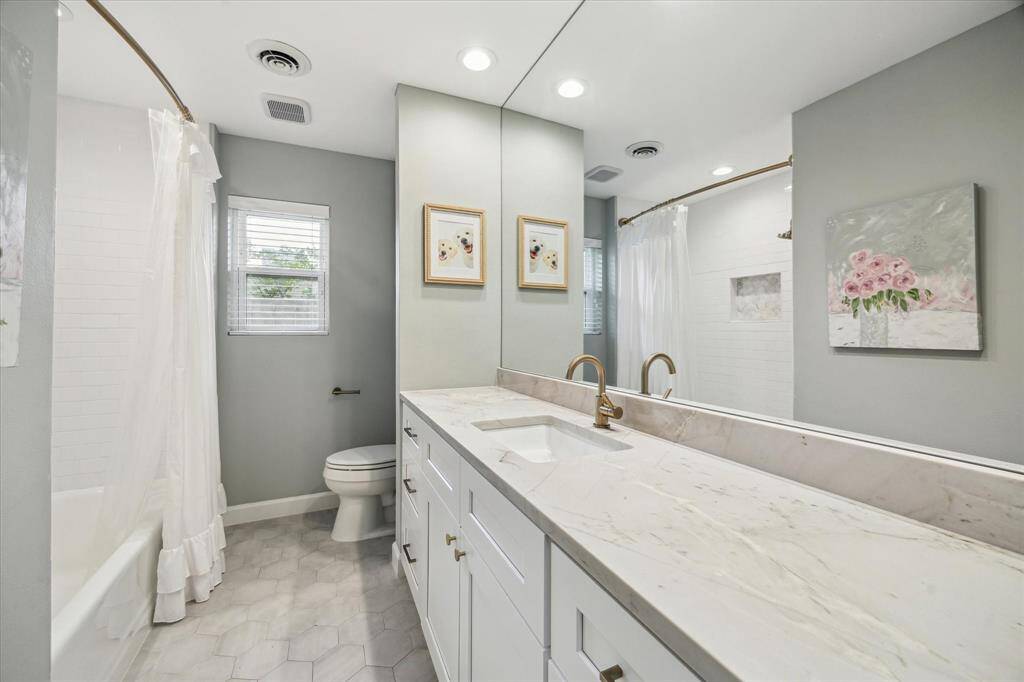 This bathroom features a sleek design with a large mirror, elegant countertop, and modern fixtures. It includes an updated bathtub with shower and light gray walls creating a clean and inviting atmosphere.