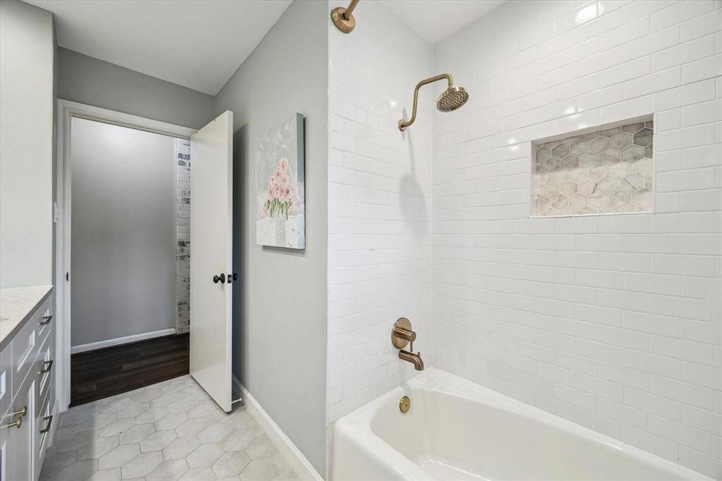 This is a modern bathroom featuring a white tiled shower with a built-in niche and bronze fixtures. The room has hexagonal floor tiles, a vanity with drawers, and soft gray walls, giving it a clean and contemporary look.