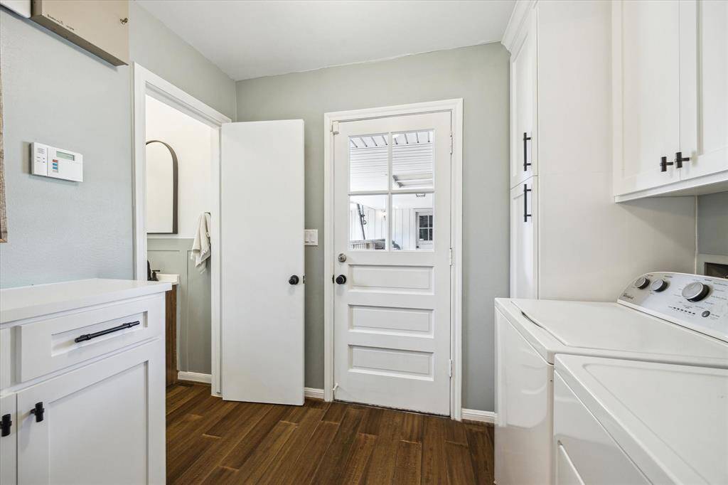 This photo showcases a bright and functional laundry room with hardwood flooring, featuring a washer and dryer, white cabinetry for storage, and a door leading outside.